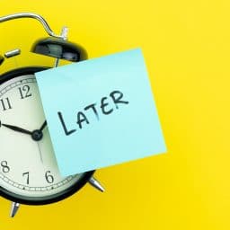 Alarm clock with a sticky note on front that says later in black marker.