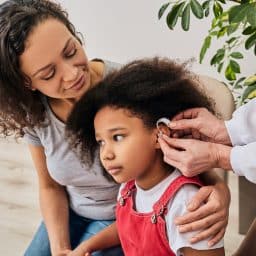 Young girl getting her hearing aid fitted with her mother by her side.