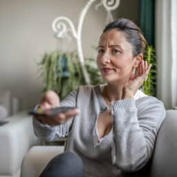 Young woman adjusting her hearing aid while watching TV.