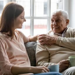 Young adult woman talking with her older father on the couch.