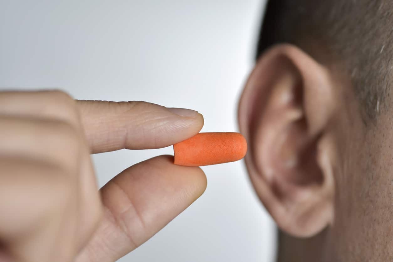 Man holds earplug to ear 
