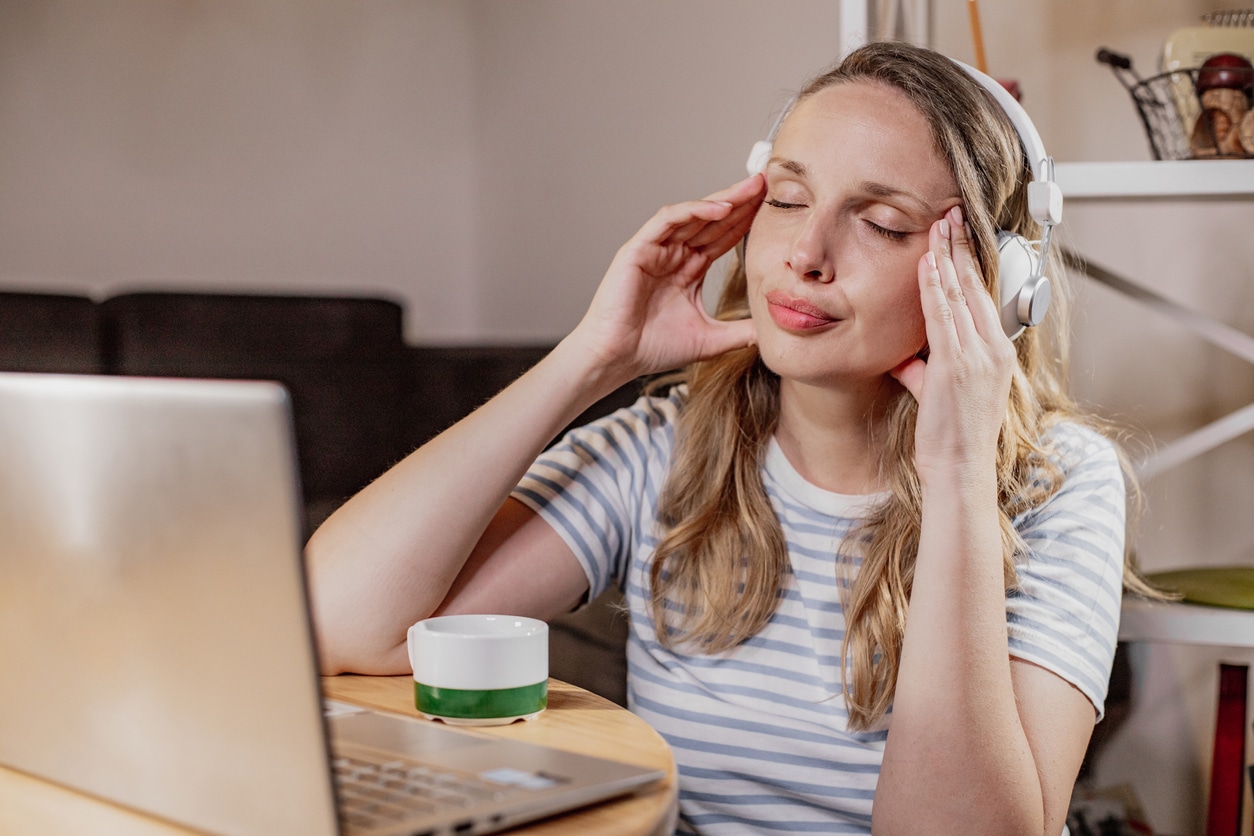 Tired woman rubbing her temples with headphones on .