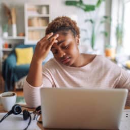 Tired at Home Office: Woman Grasps Head in Worry While Working on Laptop