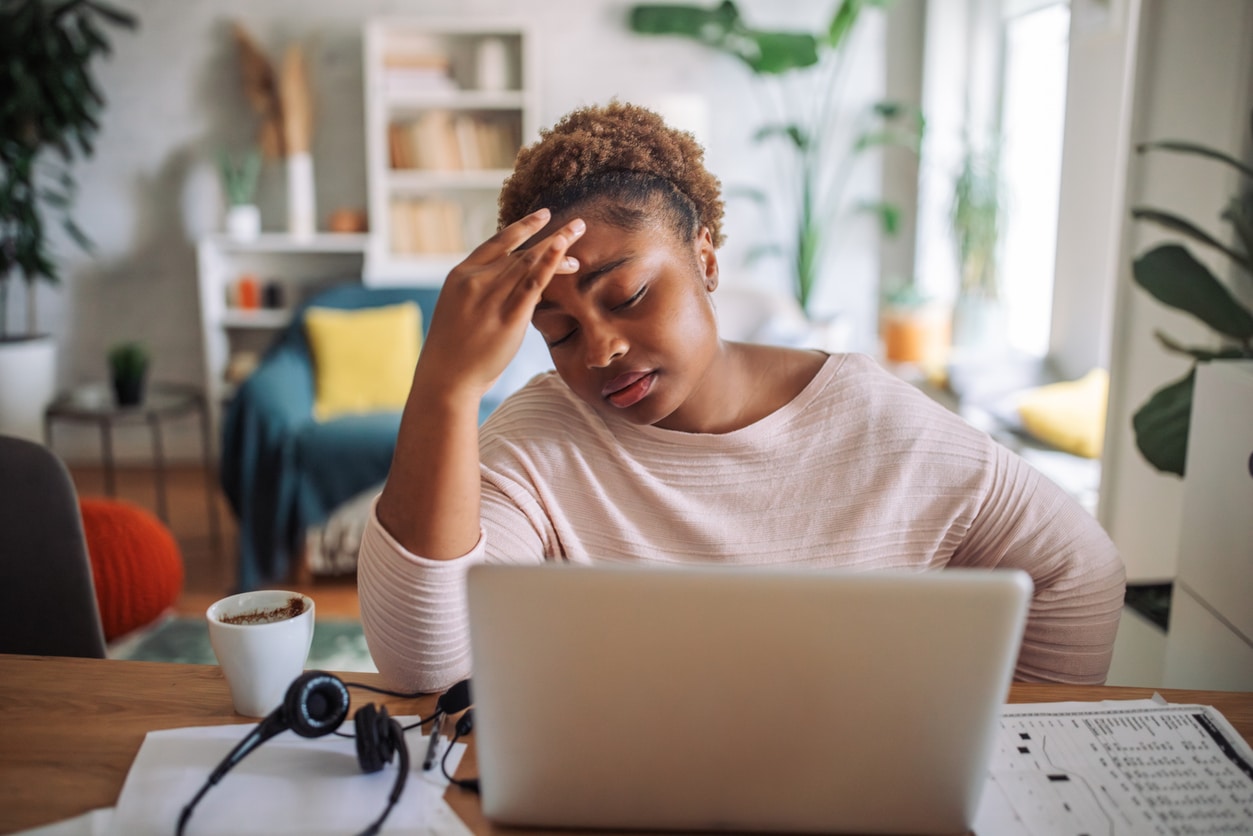 Tired at Home Office: Woman Grasps Head in Worry While Working on Laptop .