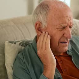 Older man holding his right ear and looking annoyed at tinnitus.