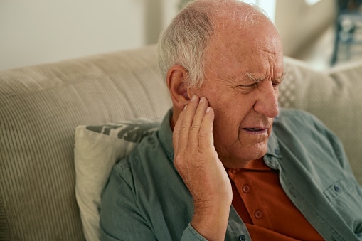 Older man holding his right ear.