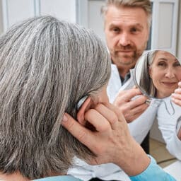 Patient looking at her new hearing aid as a doctor holds a mirror up for her.