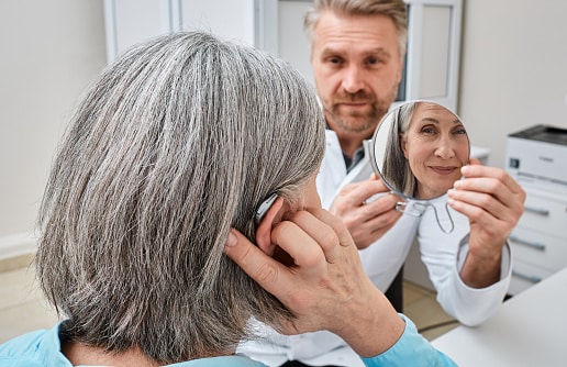 Patient looking at her new hearing aid as a doctor holds a mirror up for her.