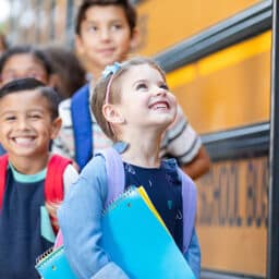 Children with backpacks and notebooks eagerly wait to board a yellow school bus for a day of learning and adventure.