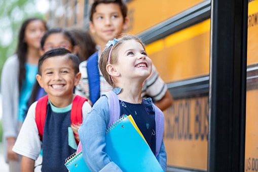 Children with backpacks and notebooks eagerly wait to board a yellow school bus for a day of learning and adventure.